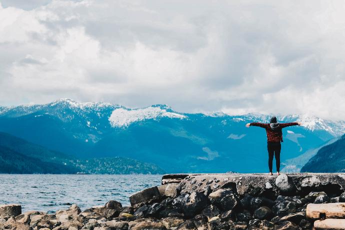 person spreading arms near water and mountain range