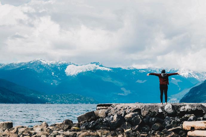 Beskrivning av bild. person spreading arms near water and mountain range